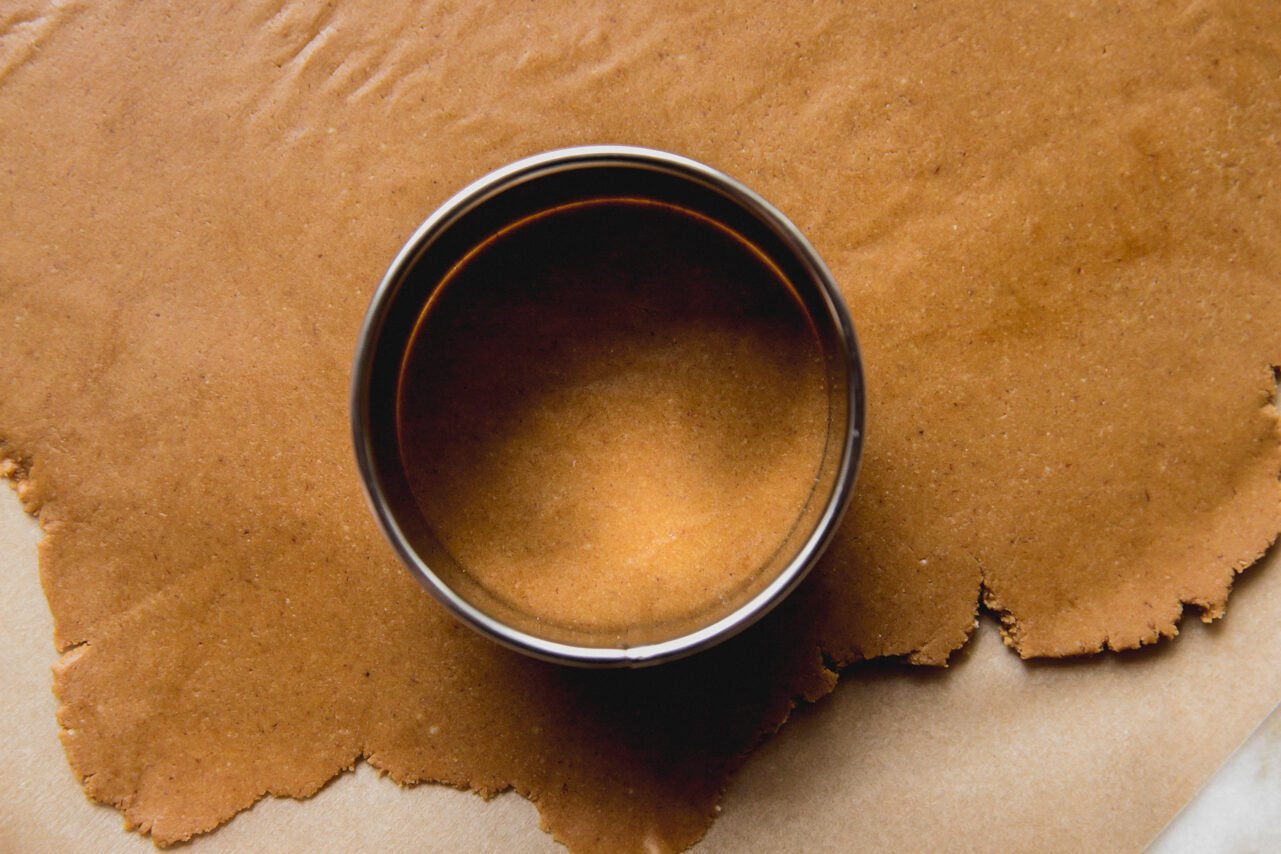 A round cookie cutter cutting a cookie out of gingerbread dough.