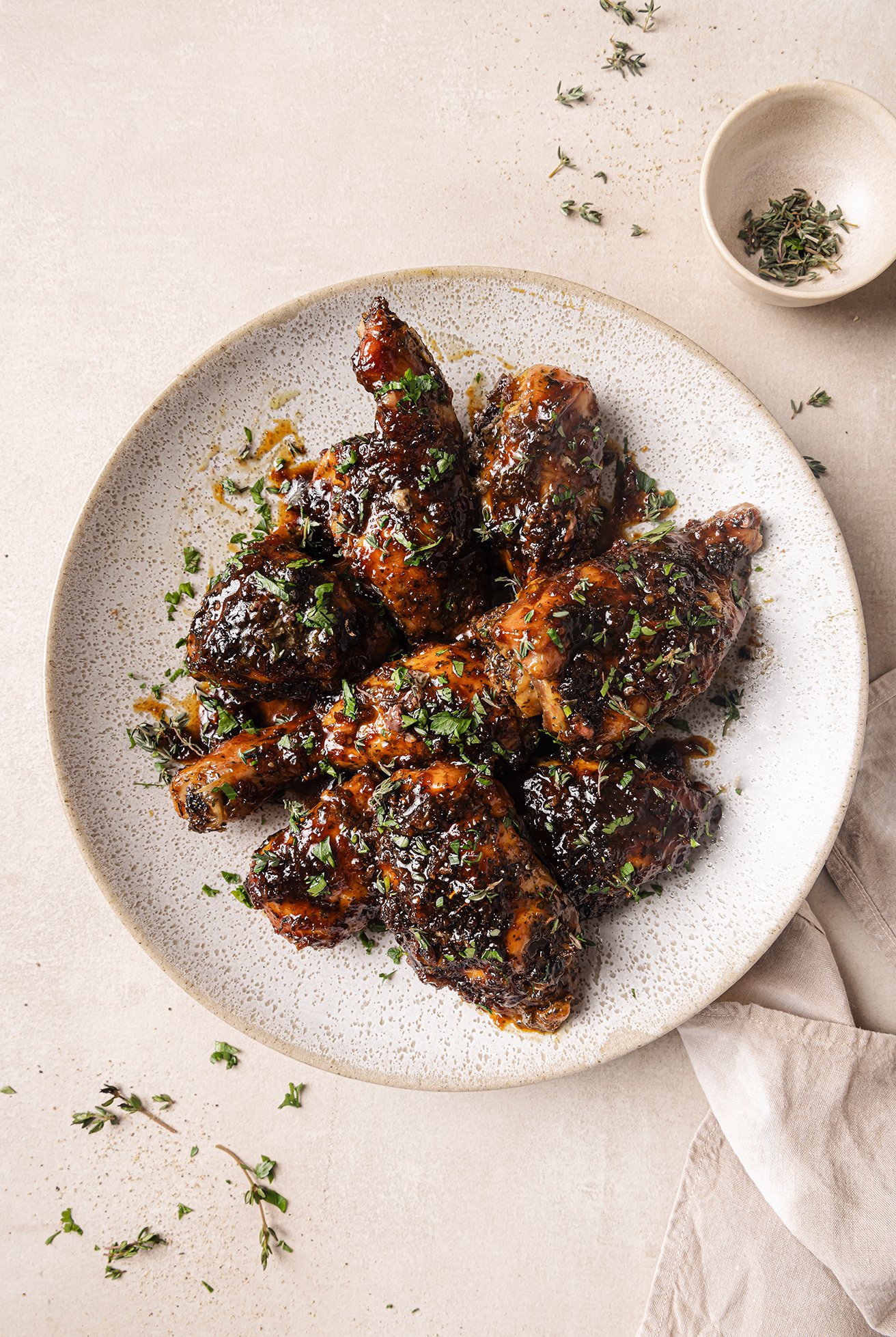 Baked turkey wings on a plate topped with thyme, with a small bowl of thyme on the side.