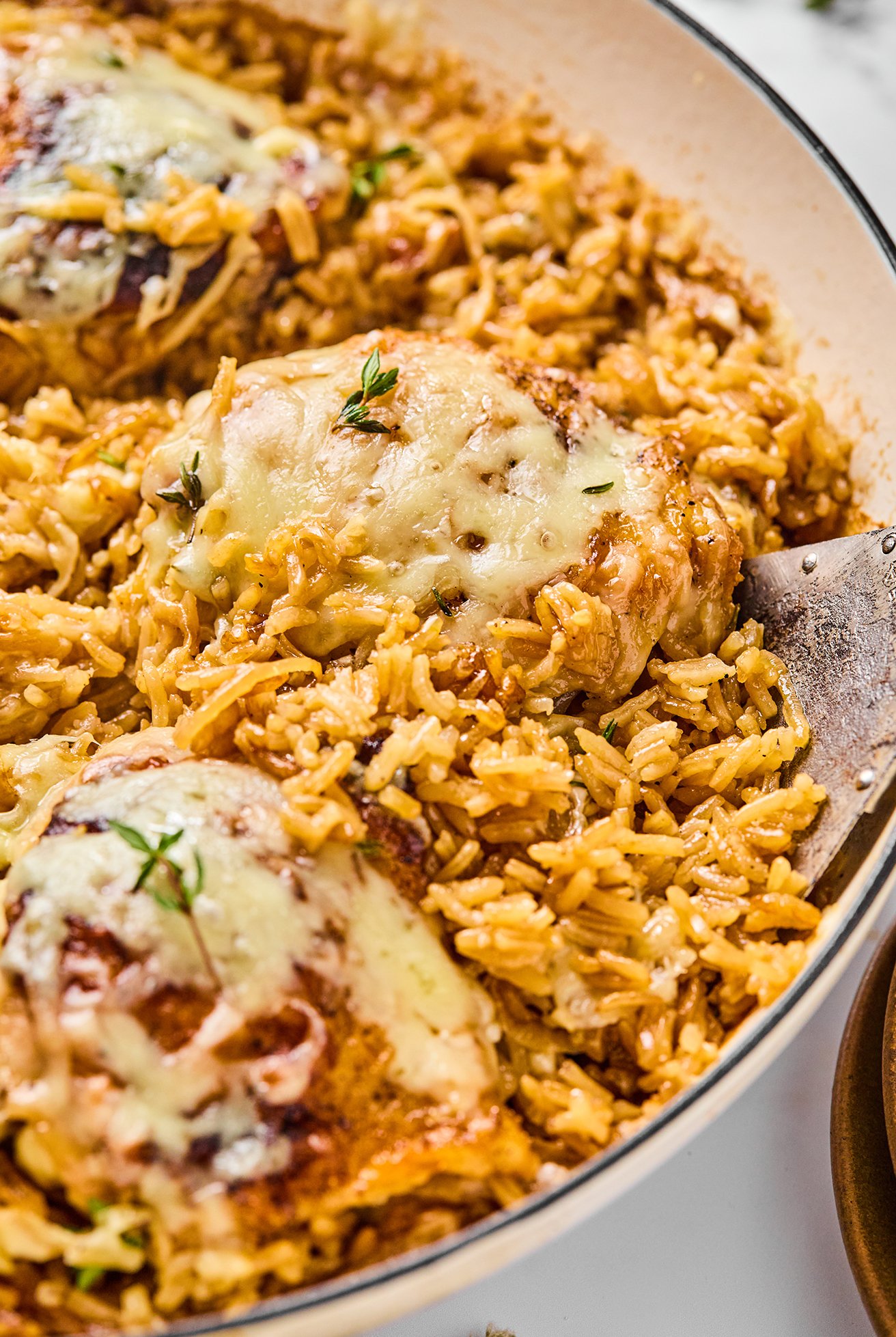 A French onion chicken thigh being taken out of the pan.