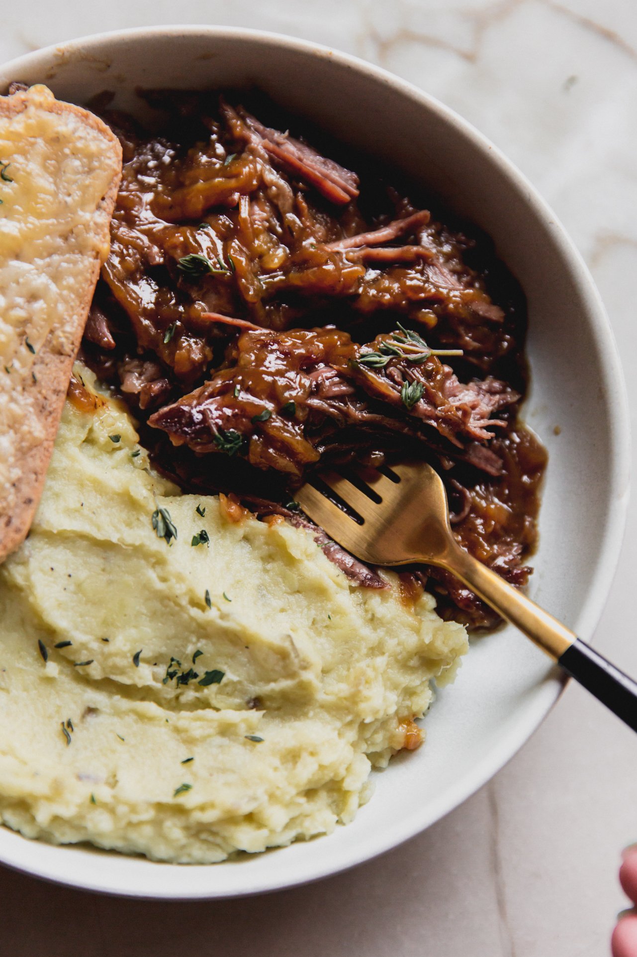 French onion pot roast in a shallow bowl with mashed sweet potato. 