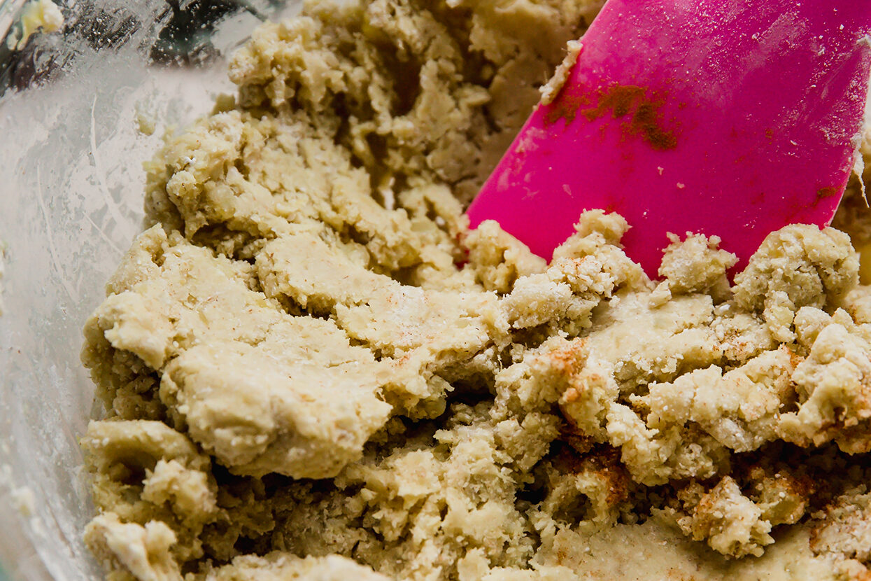 Gingerbread cinnamon roll dough in a bowl with a spoon.