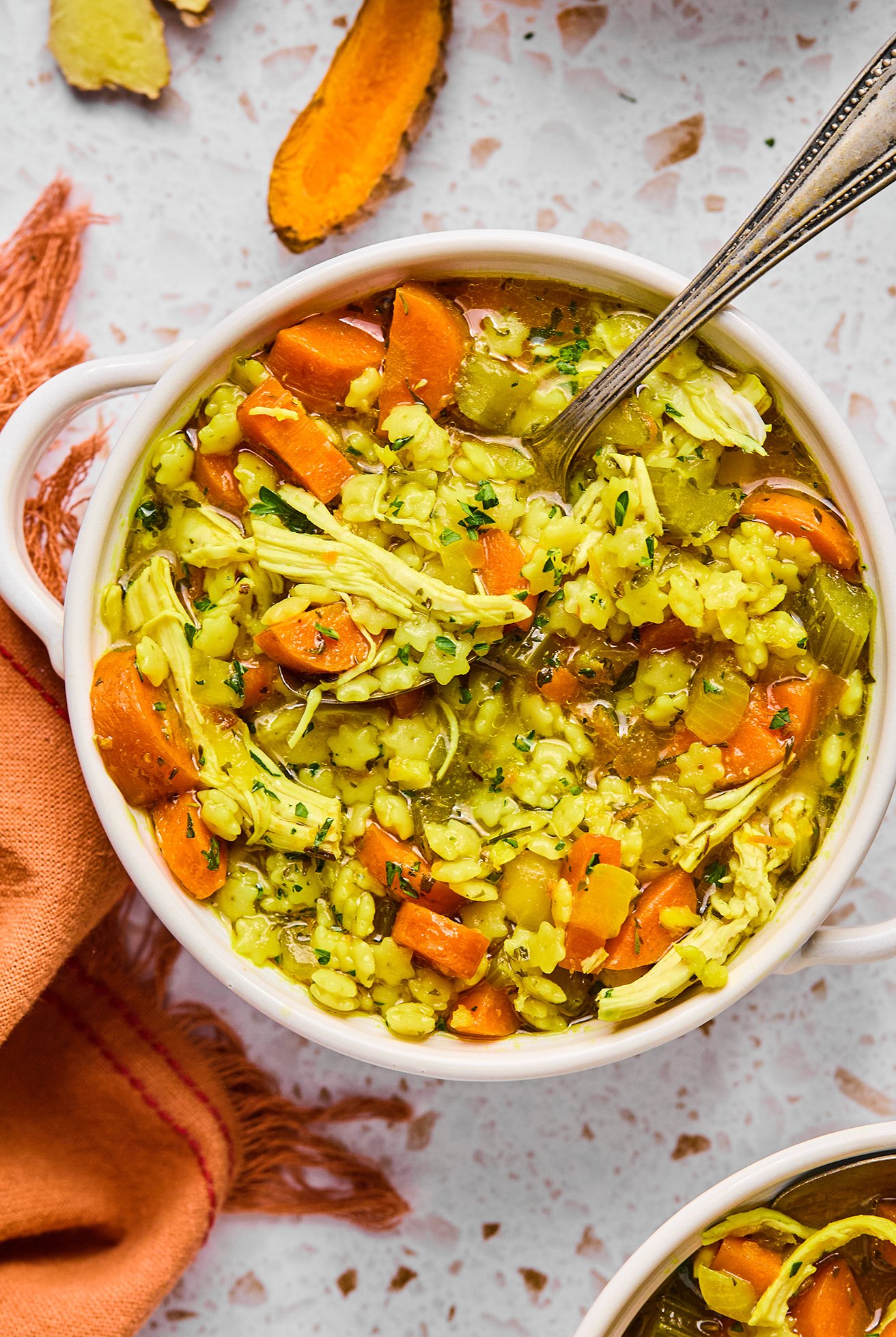 A bowl of lemon turmeric chicken noodle soup with a spoon in it ready to be eaten.