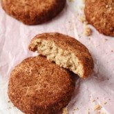 Snickerdoodle cookies on a baking tray, with one broken in half.