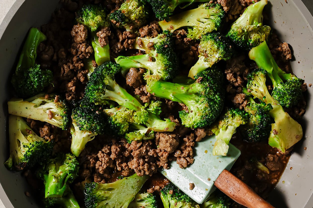 Ground beef and broccoli cooking in a pan without sauce.