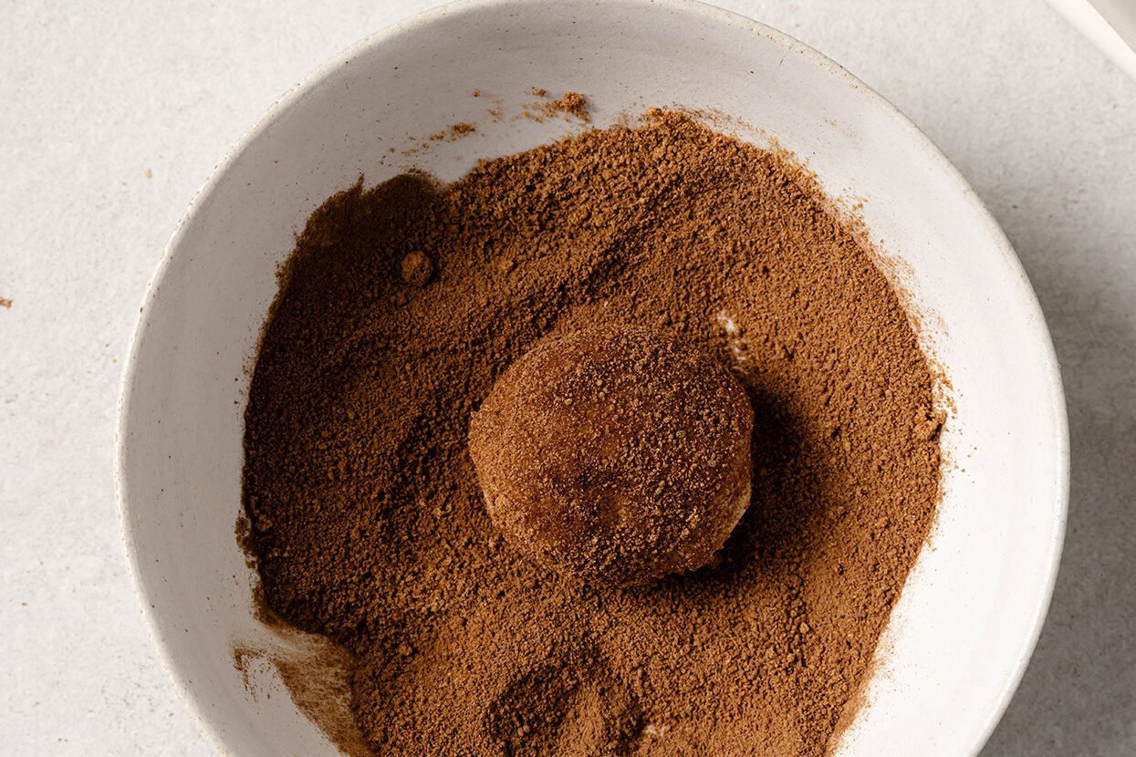 A ball of snickerdoodle dough being rolled in cinnamon sugar.