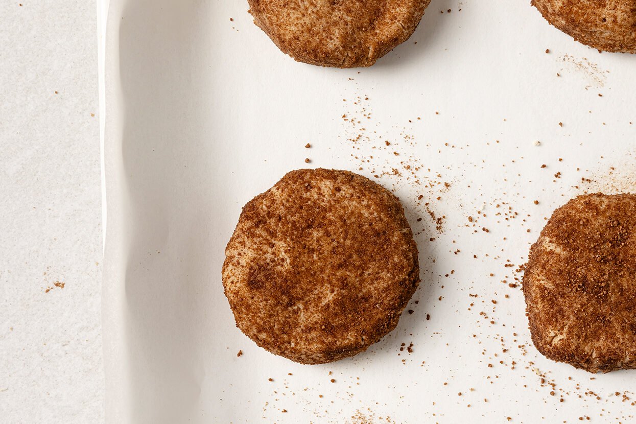 The snickerdoodle dough rolled in cinnamon sugar and flattened out on a baking sheet before baking.