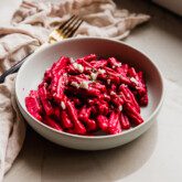 Beet pasta in a bowl topped with feta cheese and parsley.