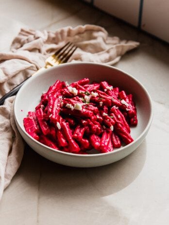 Beet pasta in a bowl topped with feta cheese and parsley.