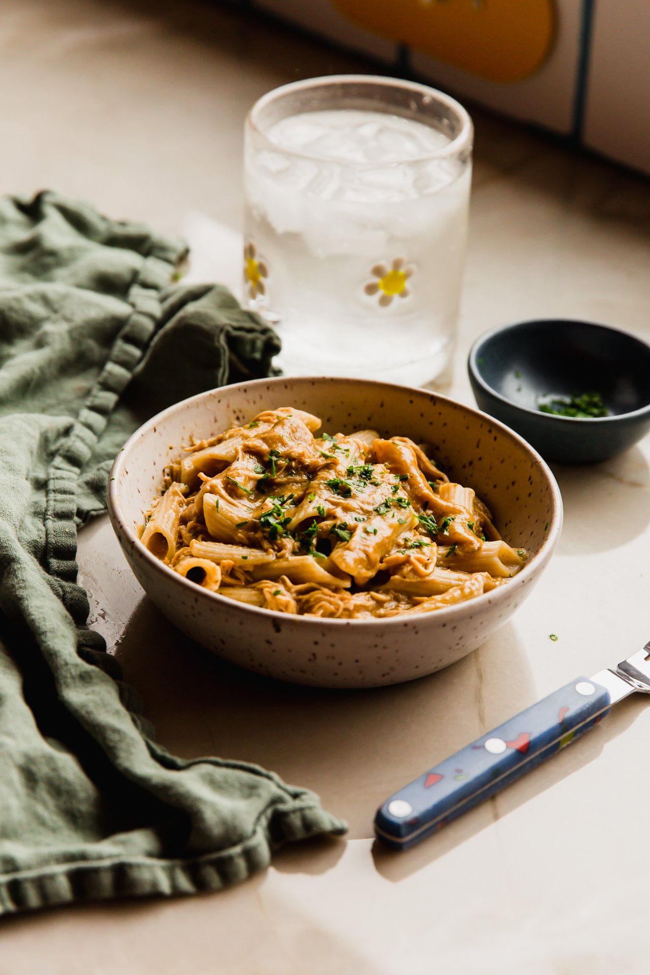 Creamy chicken pasta in a bowl with a glass of water in the background.