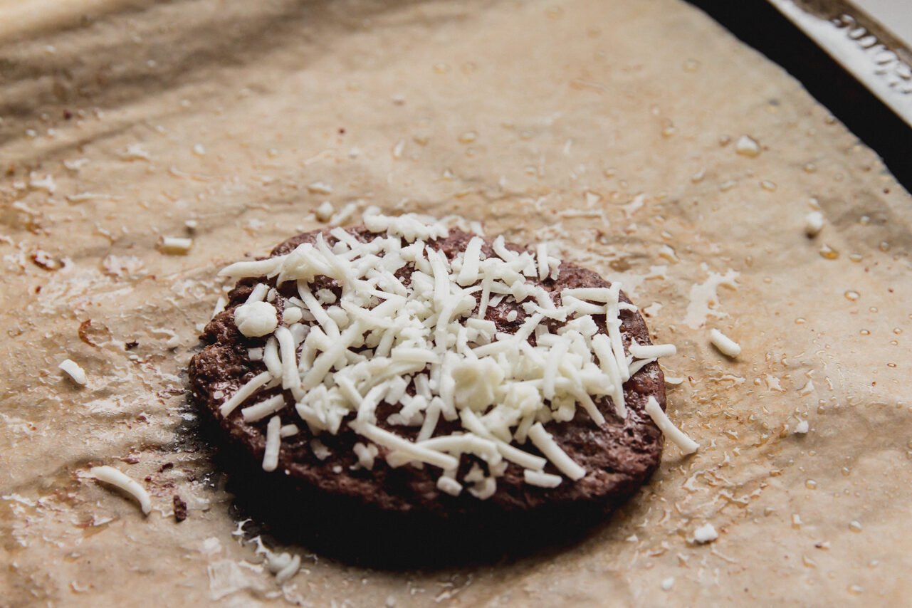 Cooked burger topped with shredded cheese.
