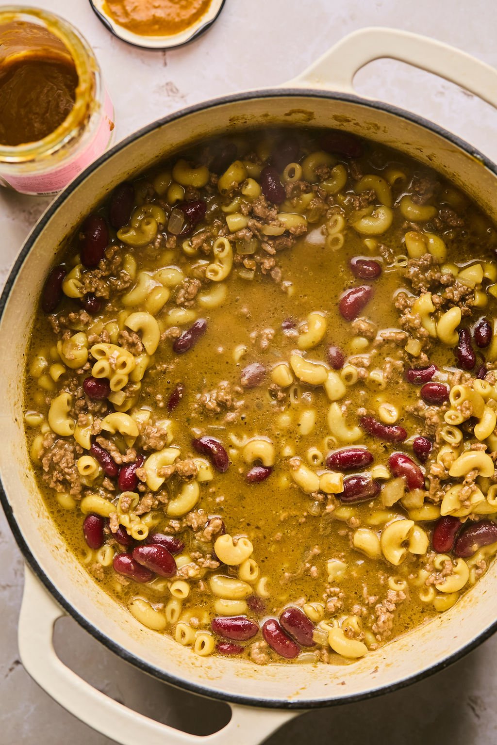 adding beans, daylight pasta sauce, chicken broth, and elbow macaroni to the pot