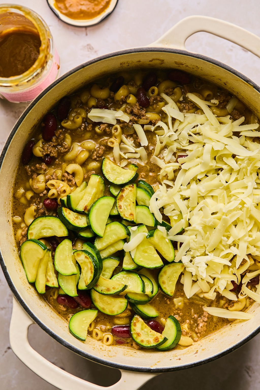 adding zucchini and cheese into the pot with chili mac