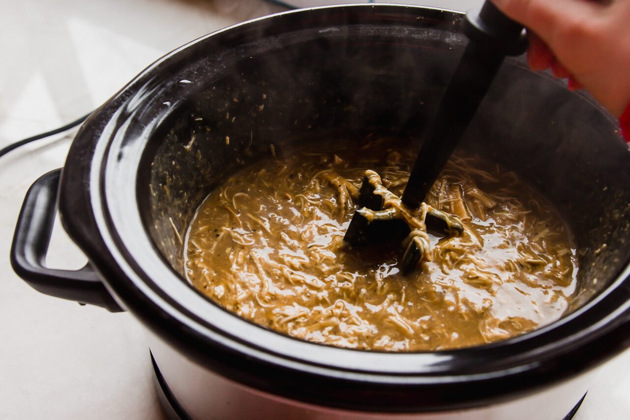 Chicken being shredded in a slow cooker into the sauce.