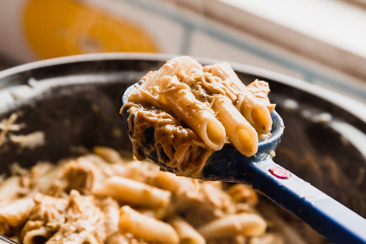 A spoon scooping creamy slow cooker chicken pasta.