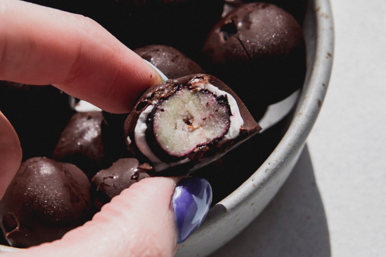 Frozen yogurt and chocolate blueberries in a bowl, with one halved from a bite. 