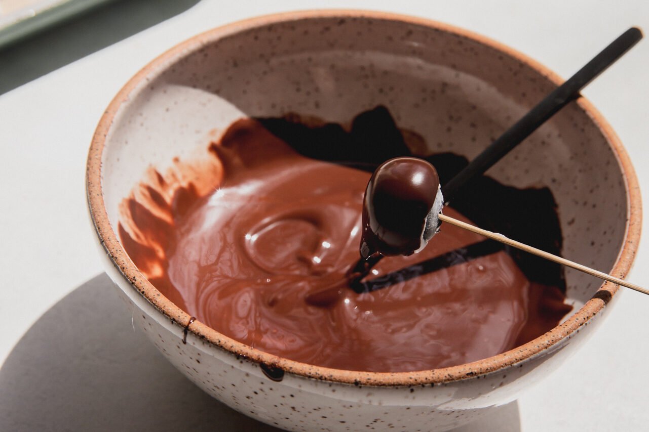 Blueberry on a toothpick being dipped in chocolate.