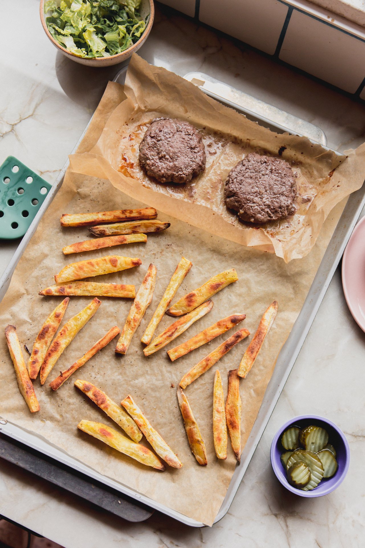 A sheet pan with fries and burgers after cooking.