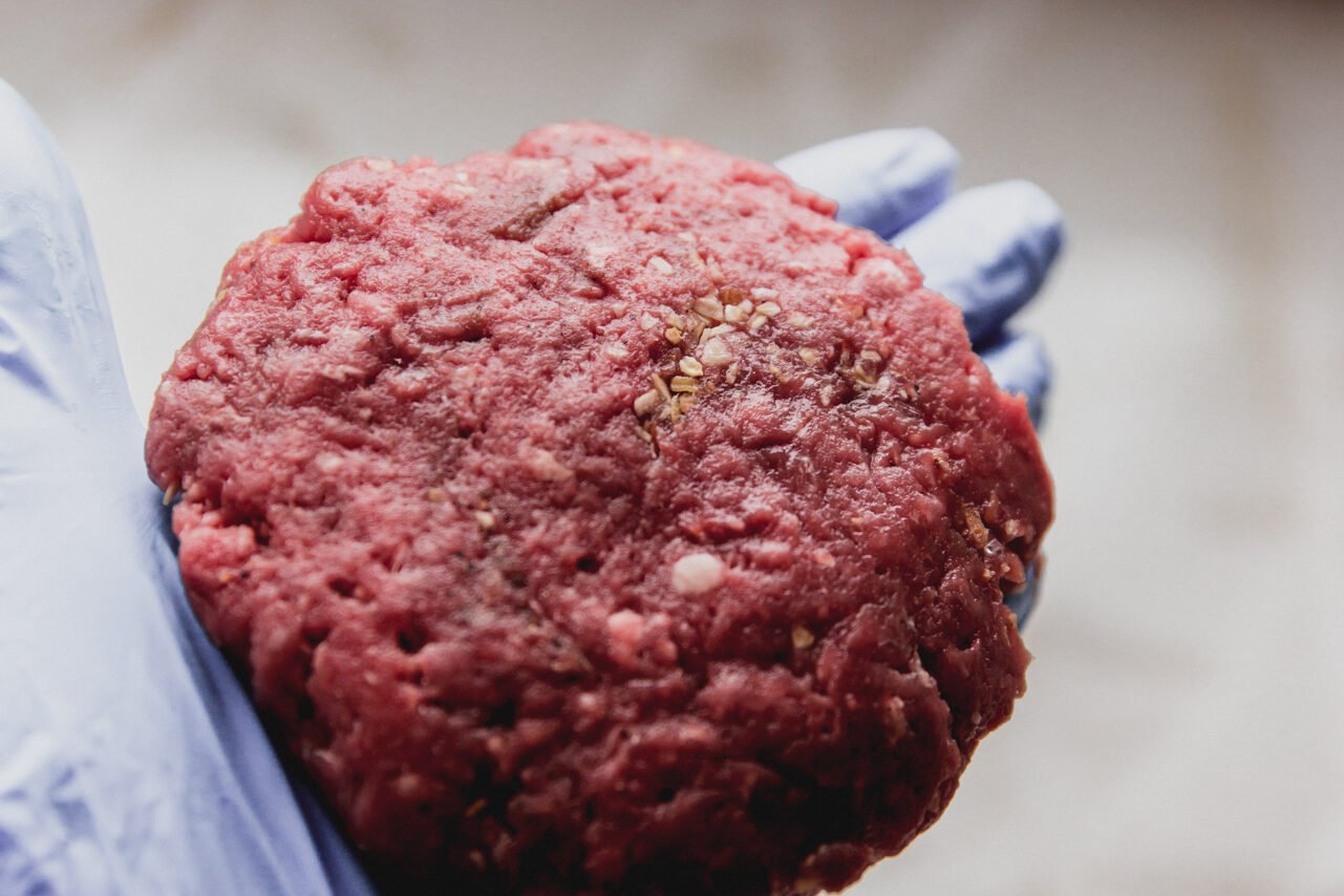 A burger formed and held in a hand before cooking.