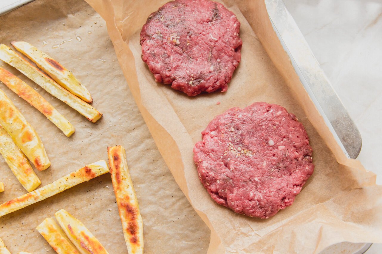 The sheet pan with the partially cooked fries and raw burgers before cooking.