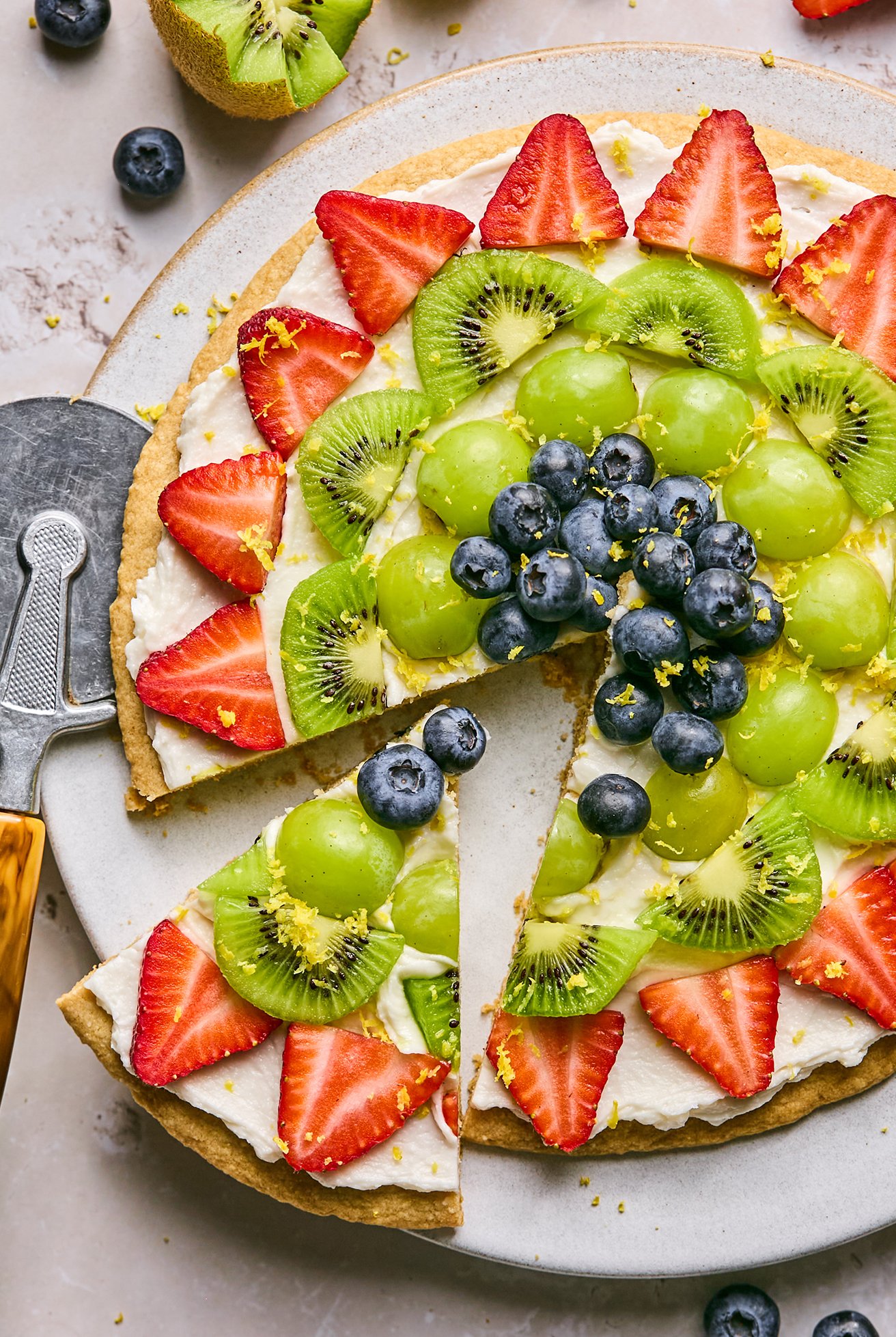 Sugar cookie fruit pizza topped with lemon zest on a large platter.
