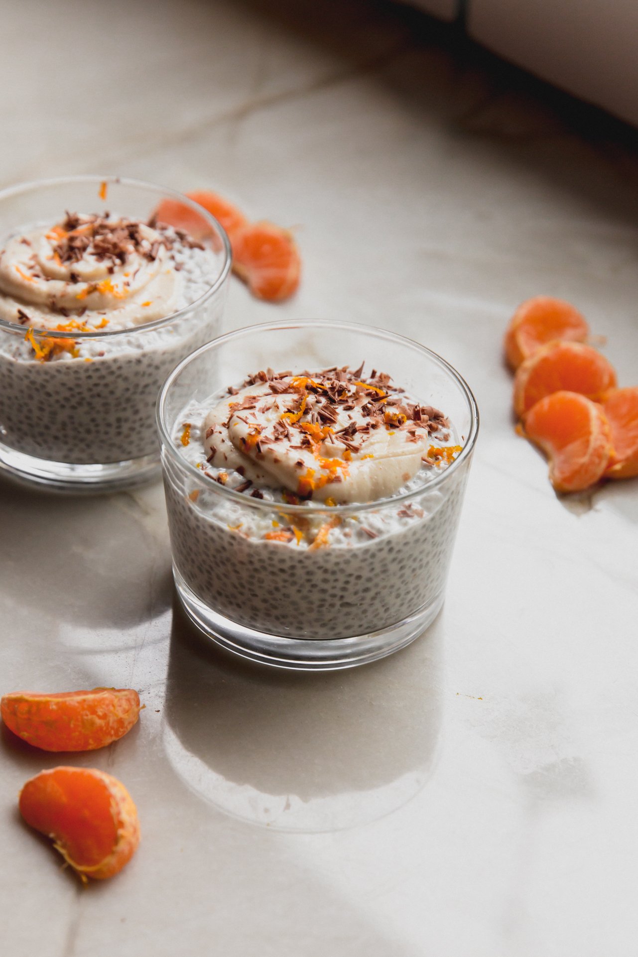 Two cups of cannoli chia seed pudding with orange segments on a counter.