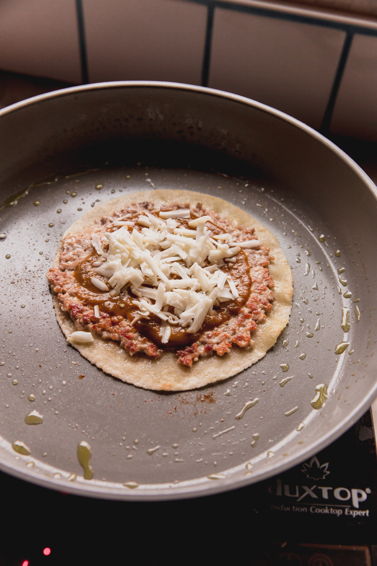 A chicken parm smash burger in a pan after cooking, topped iwth cheese.