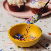 homemade sprinkles in a yellow bowl with a black spoon.