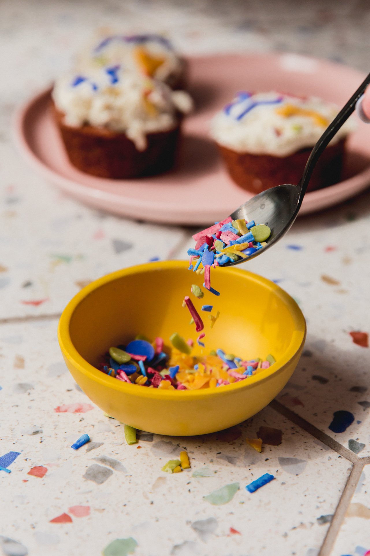 A spoon dropping homemade sprinkles into a bowl.