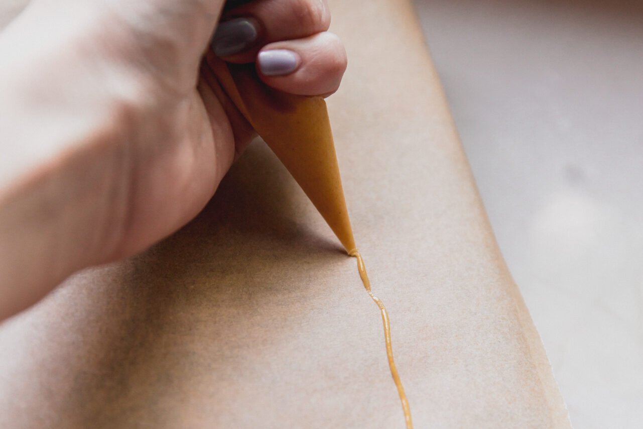 A hand piping a yellow tube across parchment paper.