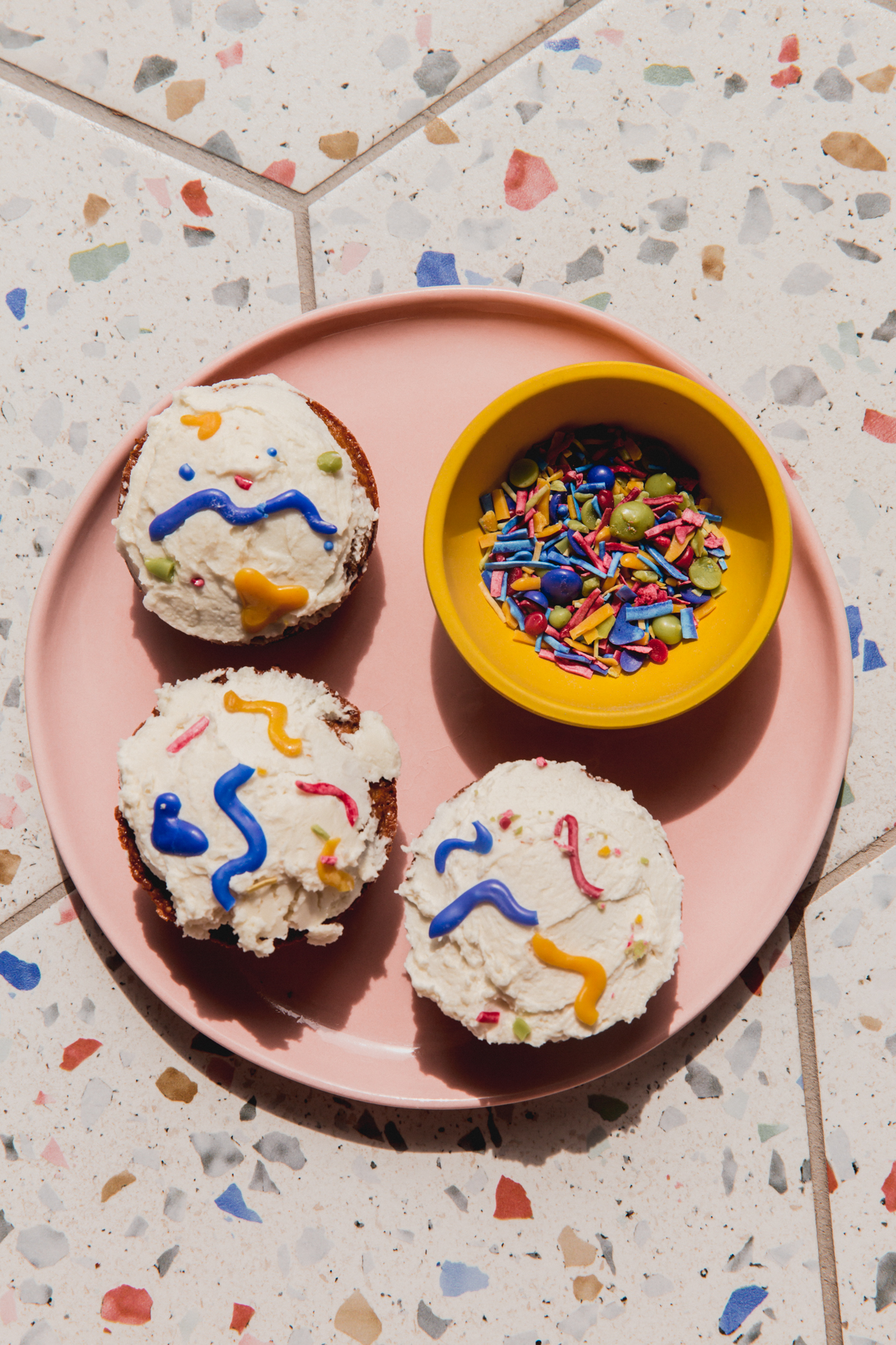 A plate with cupcakes decorated in homemade sprinkles and a bowl of homemade sprinkles.