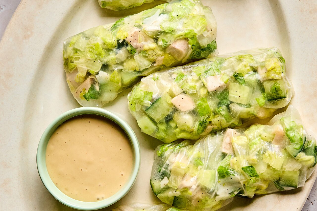A platter with 5 chicken caesar salad rice paper rolls and caesar dressing for dipping.