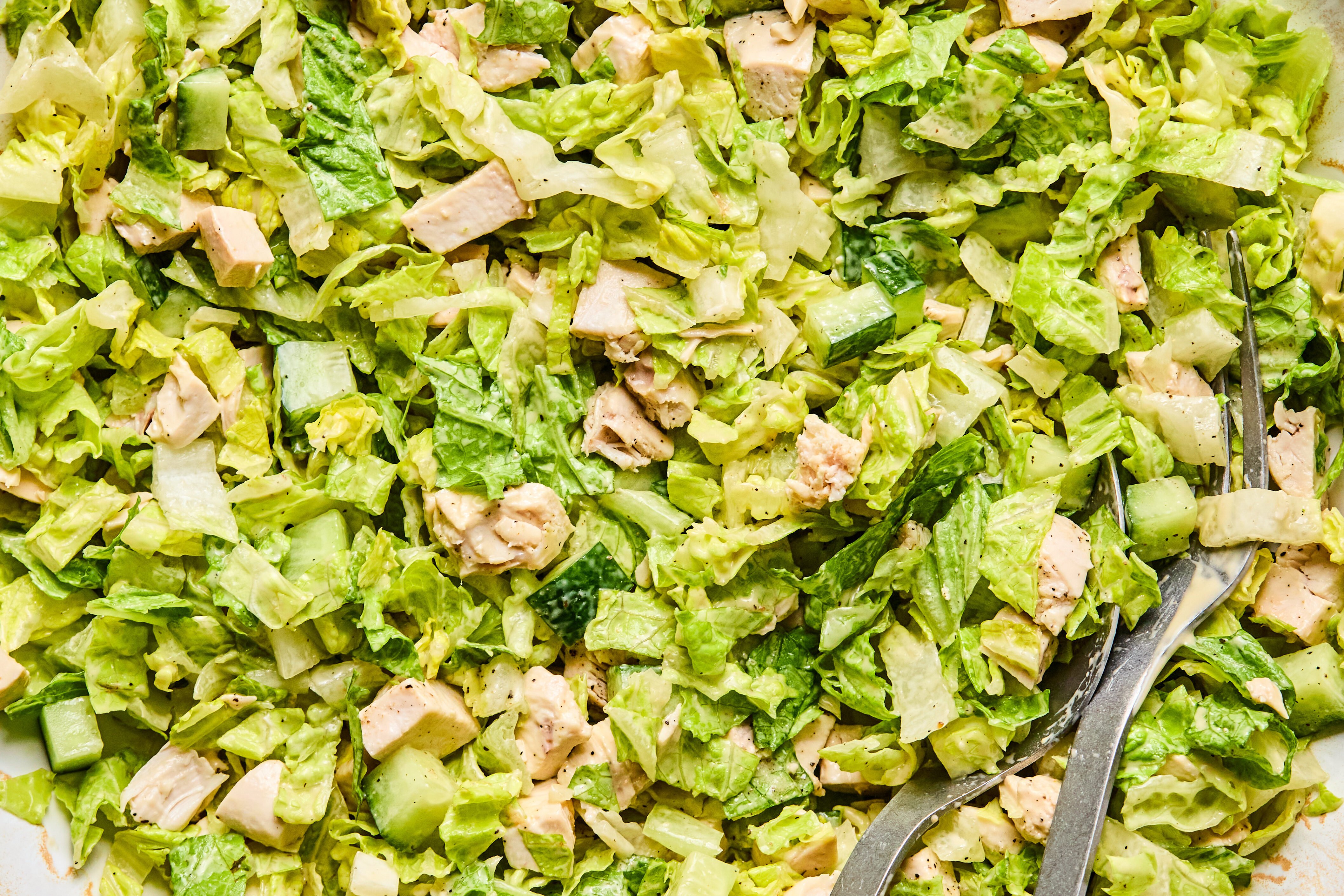 The chicken caesar salad mixed with the dressing in a large bowl.