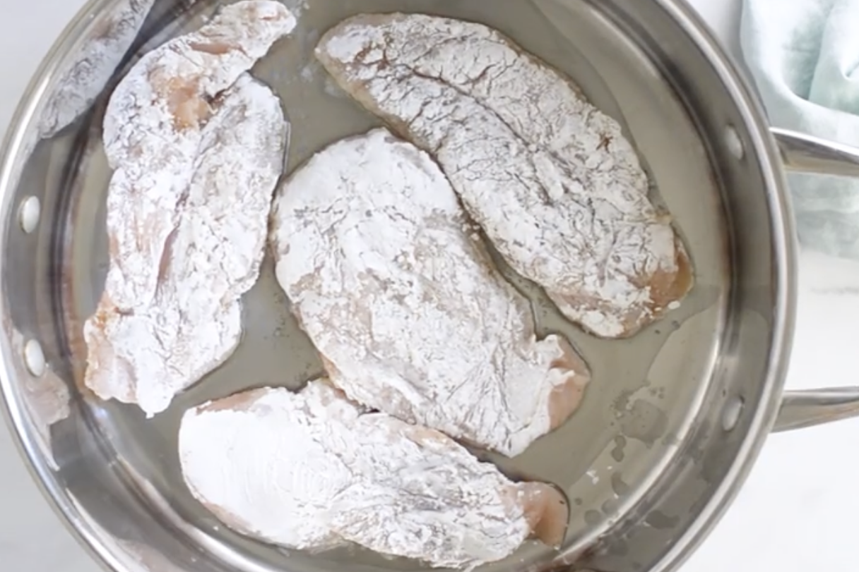Chicken breast coated in arrowroot starch in a pan.