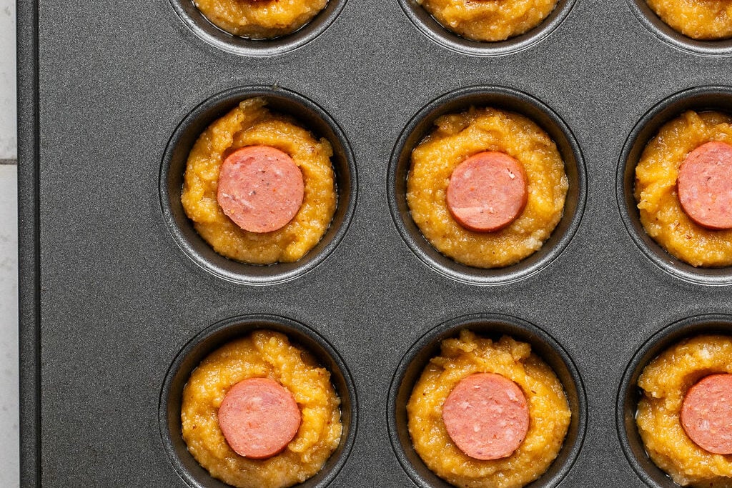 Corn dog muffins unbaked in a muffin tin.