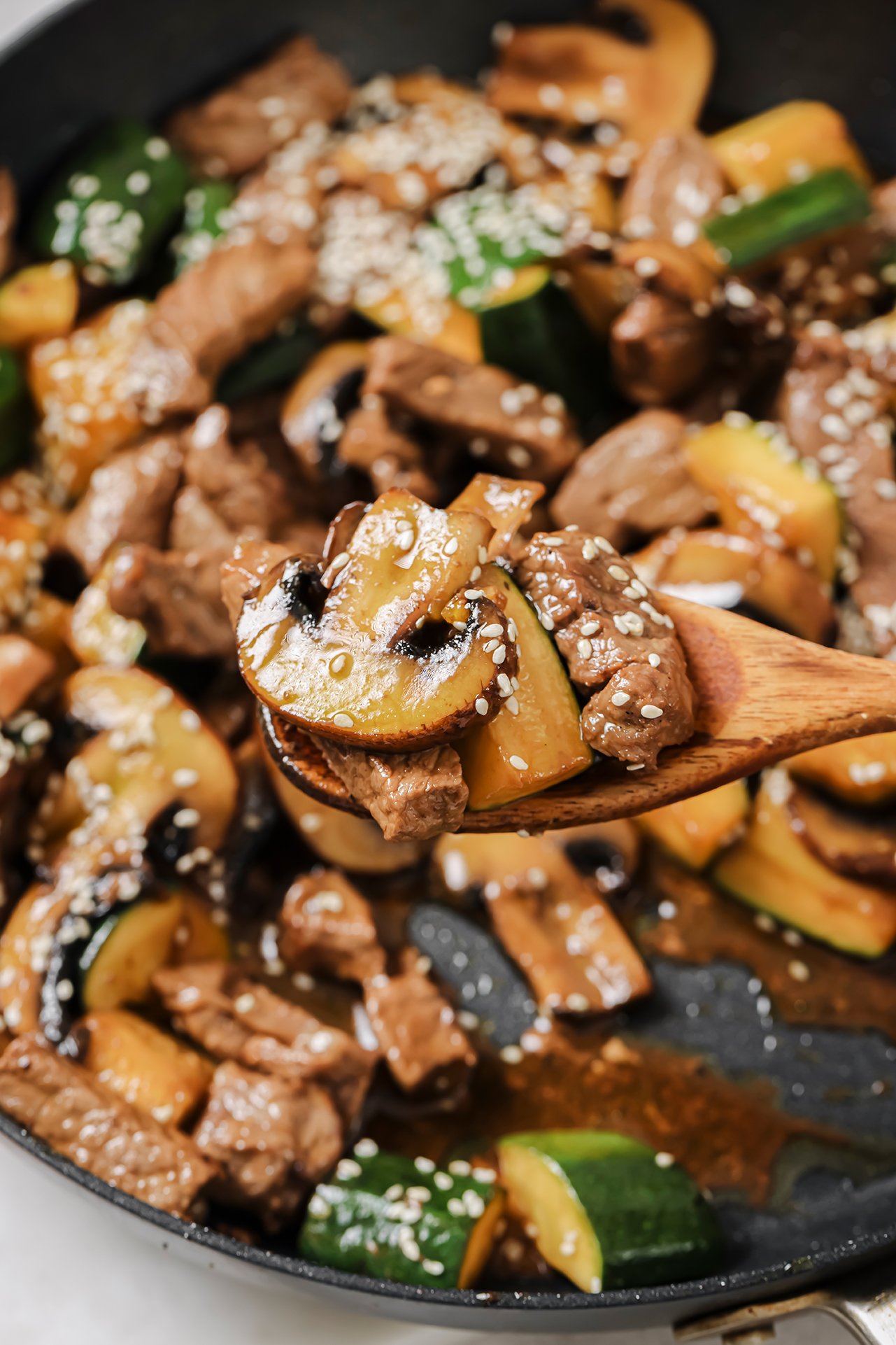 A wooden spooning pulling a bite of hibachi steak bites with zucchini and mushrooms out of a pan.
