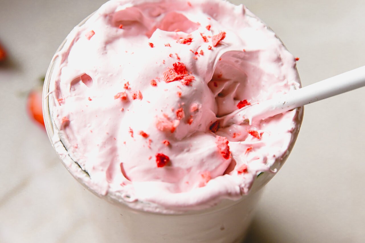 A spoon dipping into a jar of strawberry marshmallow fluff.