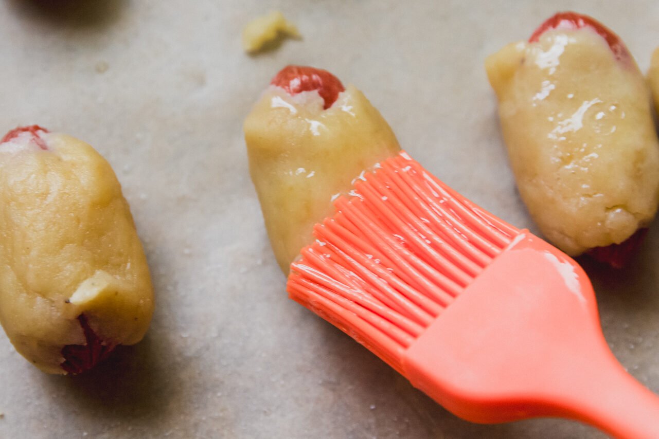 Pigs in a blanket being brushed with egg wash.