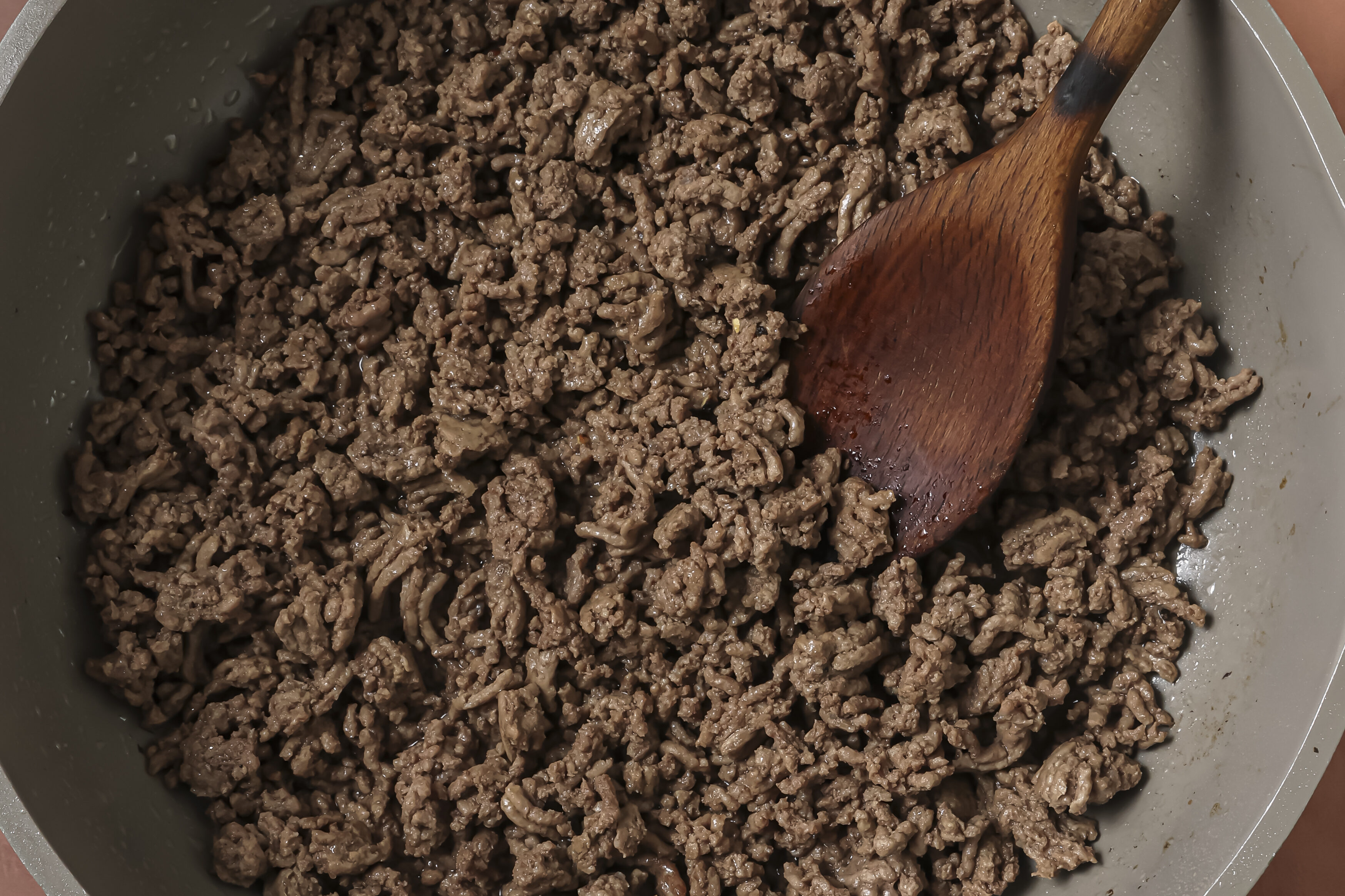 A wooden spoon browning the ground beef.