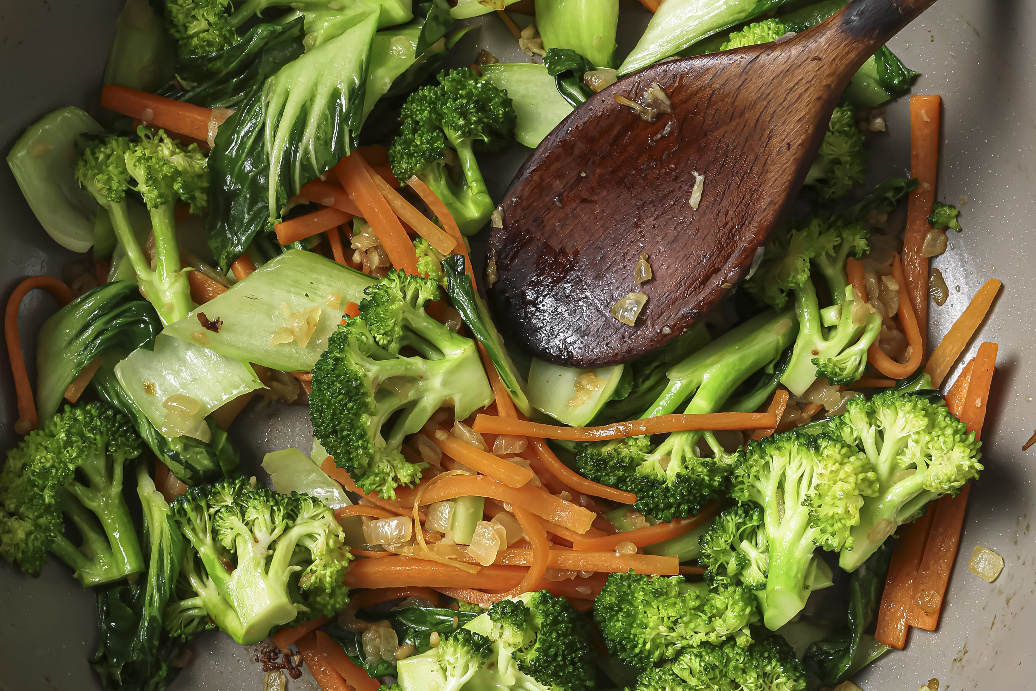 A wooden spoon sauting vegetables.