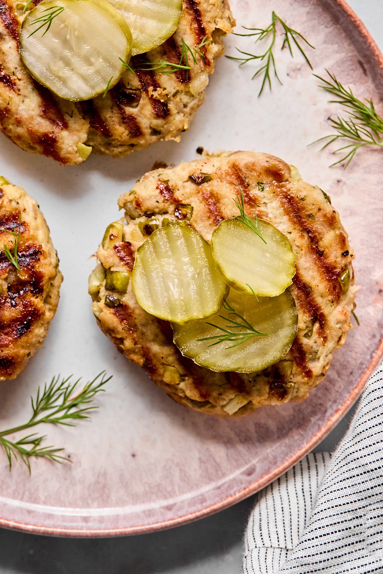 Ground chicken burgers on a platter topped with pickles.