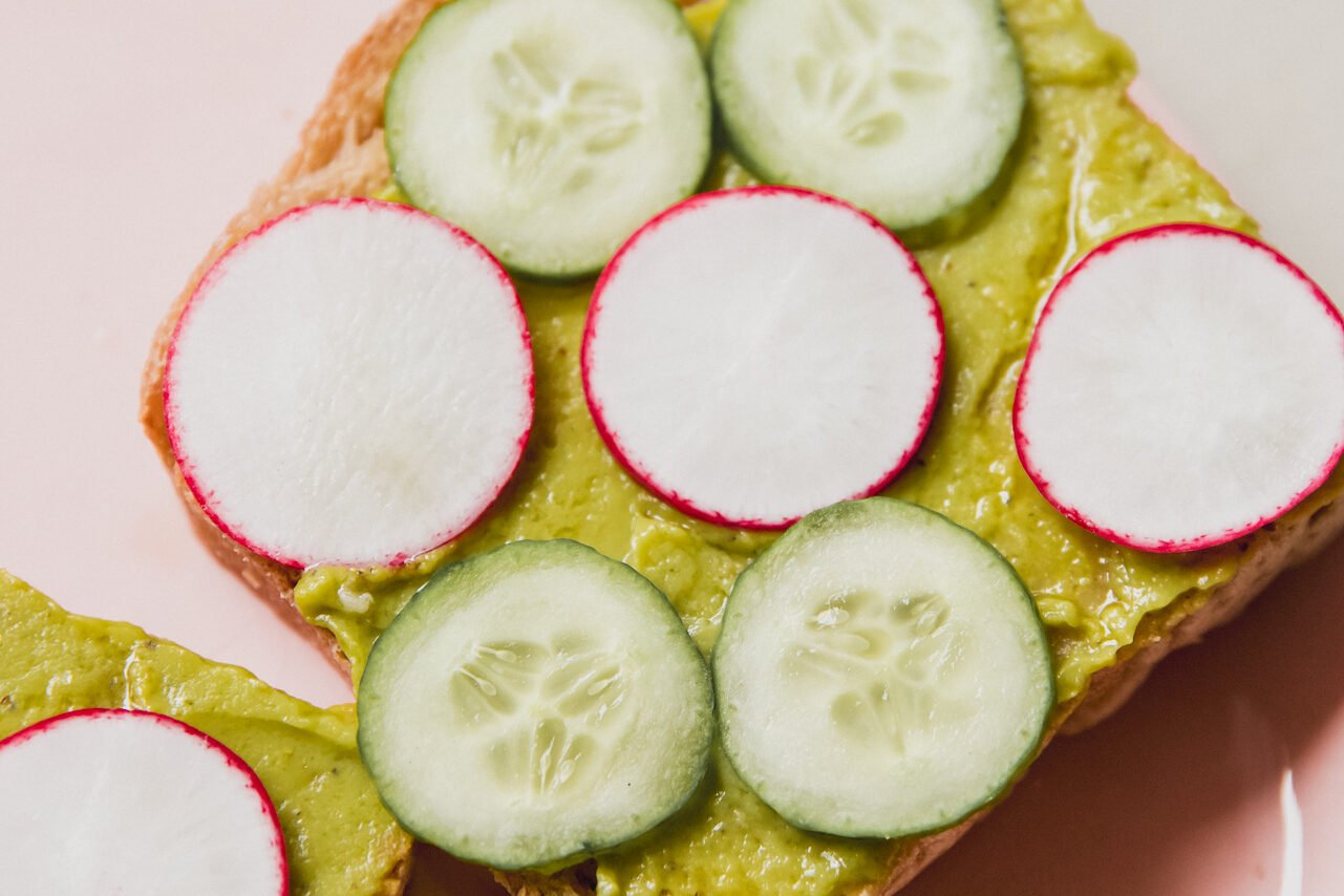 A piece of toasts with avocado, cucumbers, and radish on top.