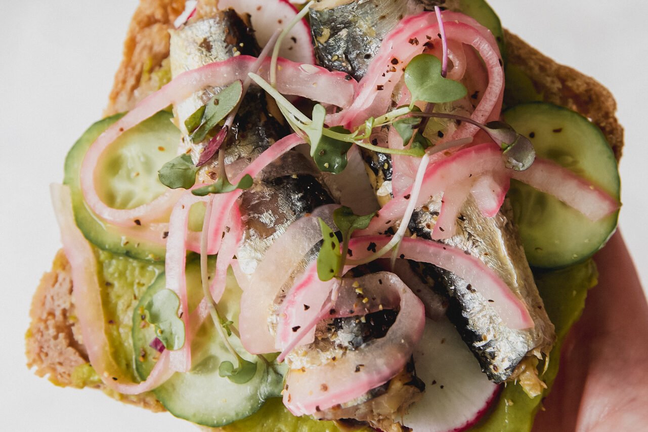 A piece of sardine toast with pickled onions and salt on top.