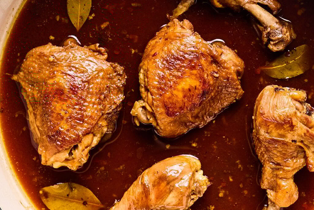 The chicken simmering in the sauce in a pan.