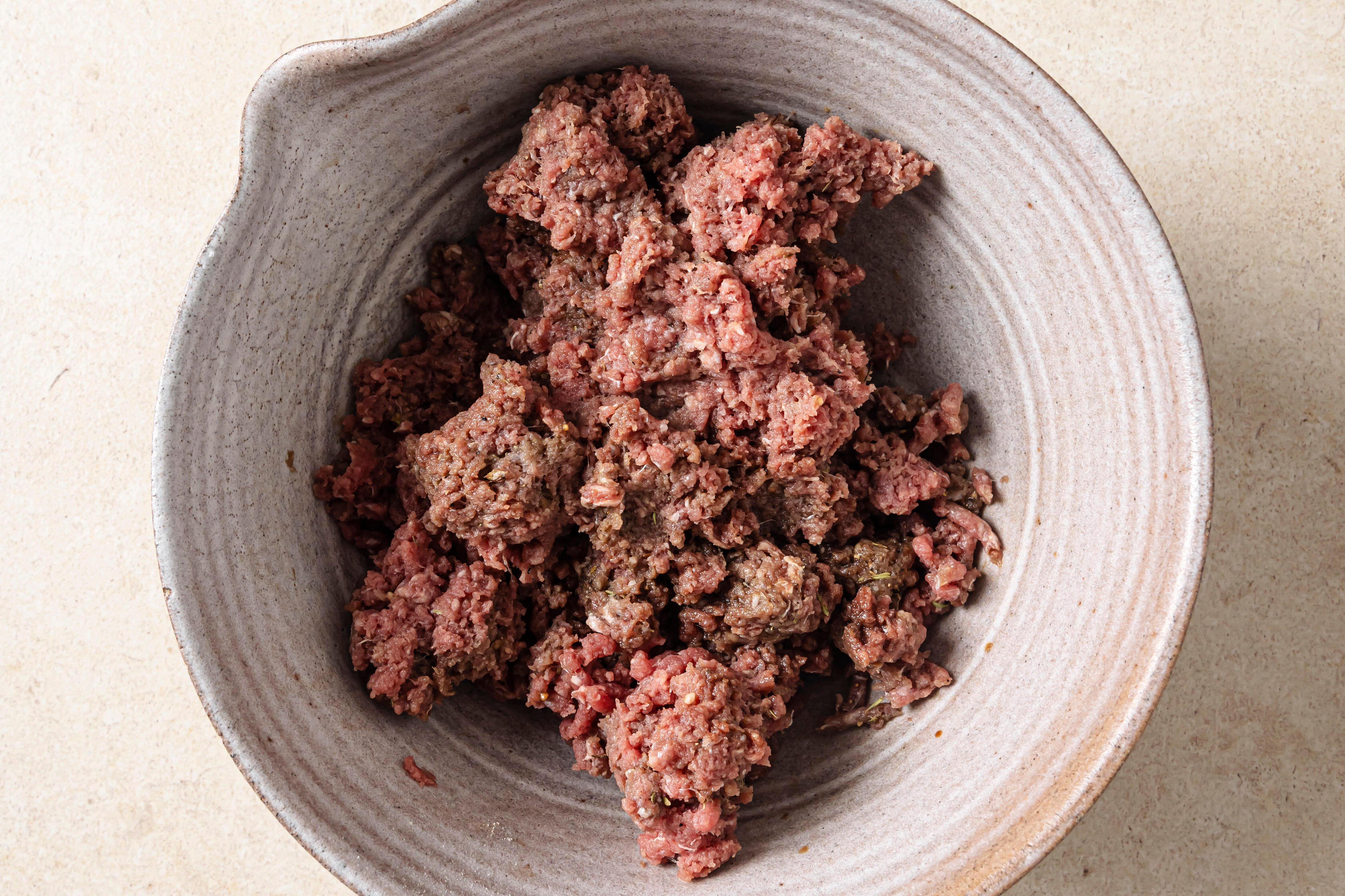 The ground beef mixing with spices in a bowl.