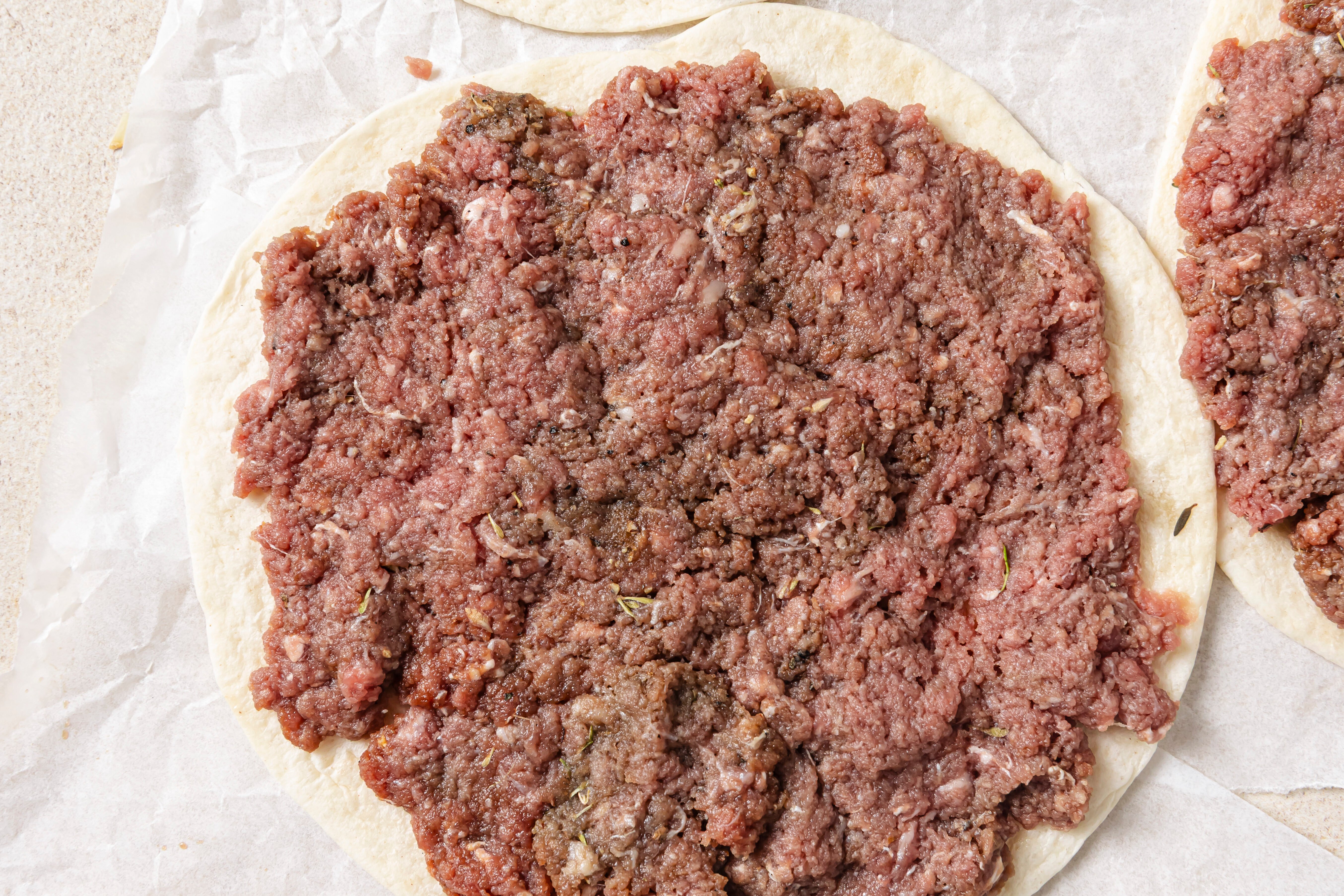Ground beef being spread on a tortilla before cooking.