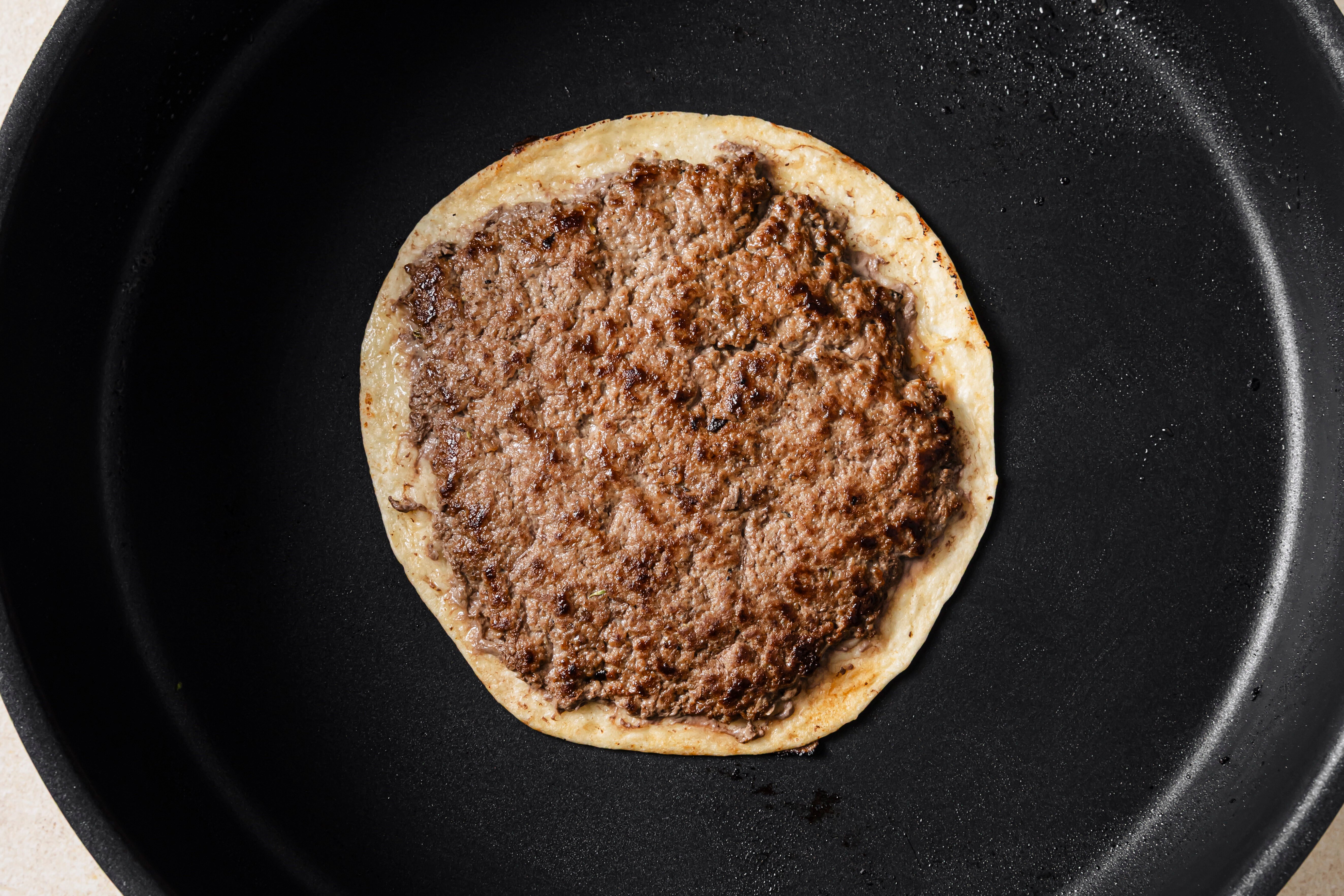 One smashburger taco cooking in a pan.