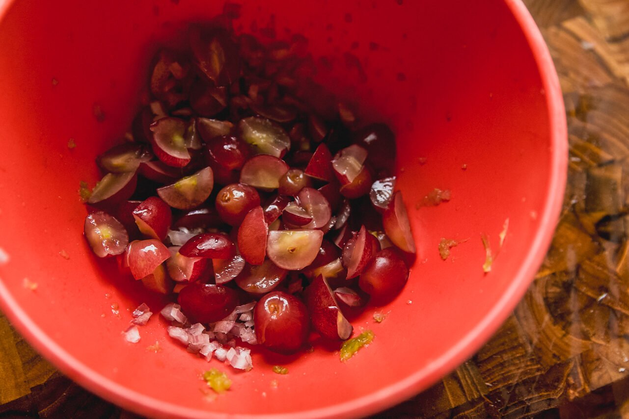 A bowl with grapes, shallots, and celery prepped in it.