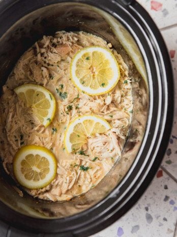 Slow cooker Greek chicken in the slow cooker topped with lemon slices.