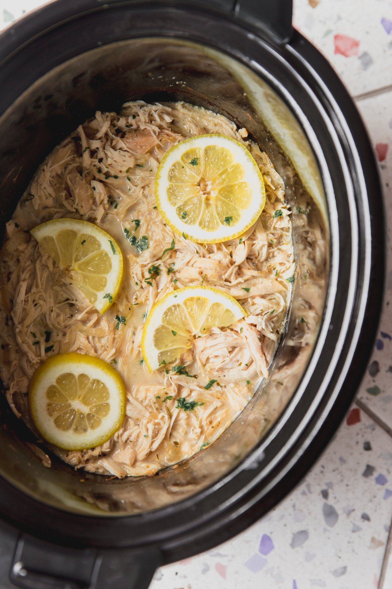 Slow cooker Greek chicken in the slow cooker topped with lemon slices.