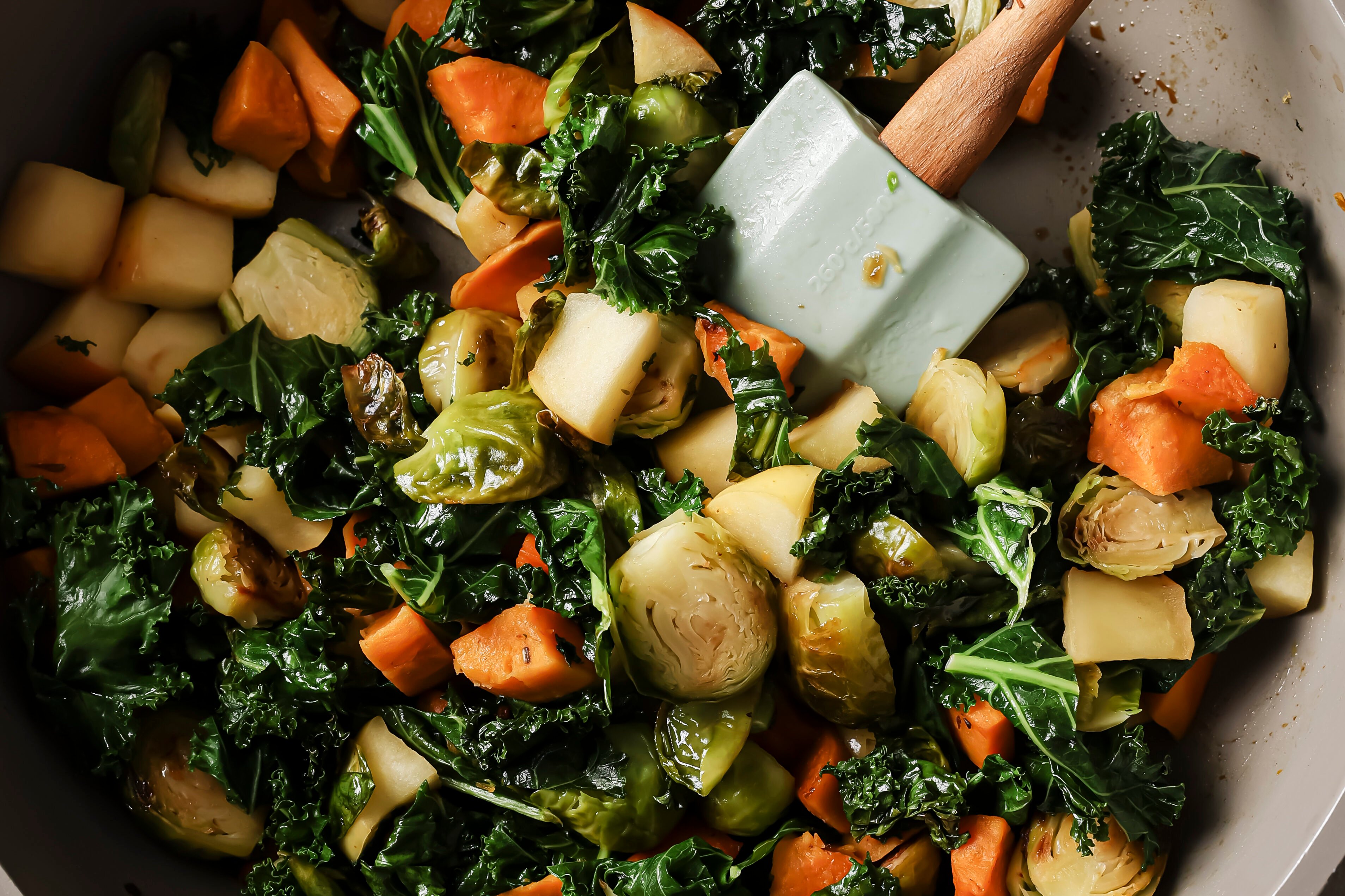 The kale and apples being added to the pan with other vegetables to saute.